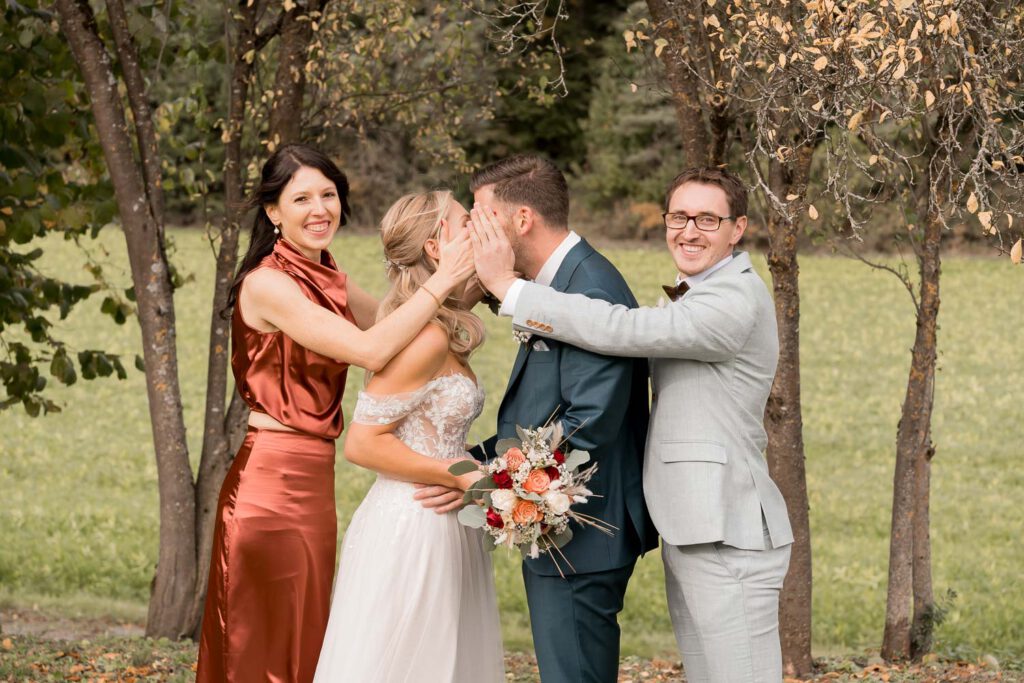 brautpaar kuss hinter haenden trauzeugen